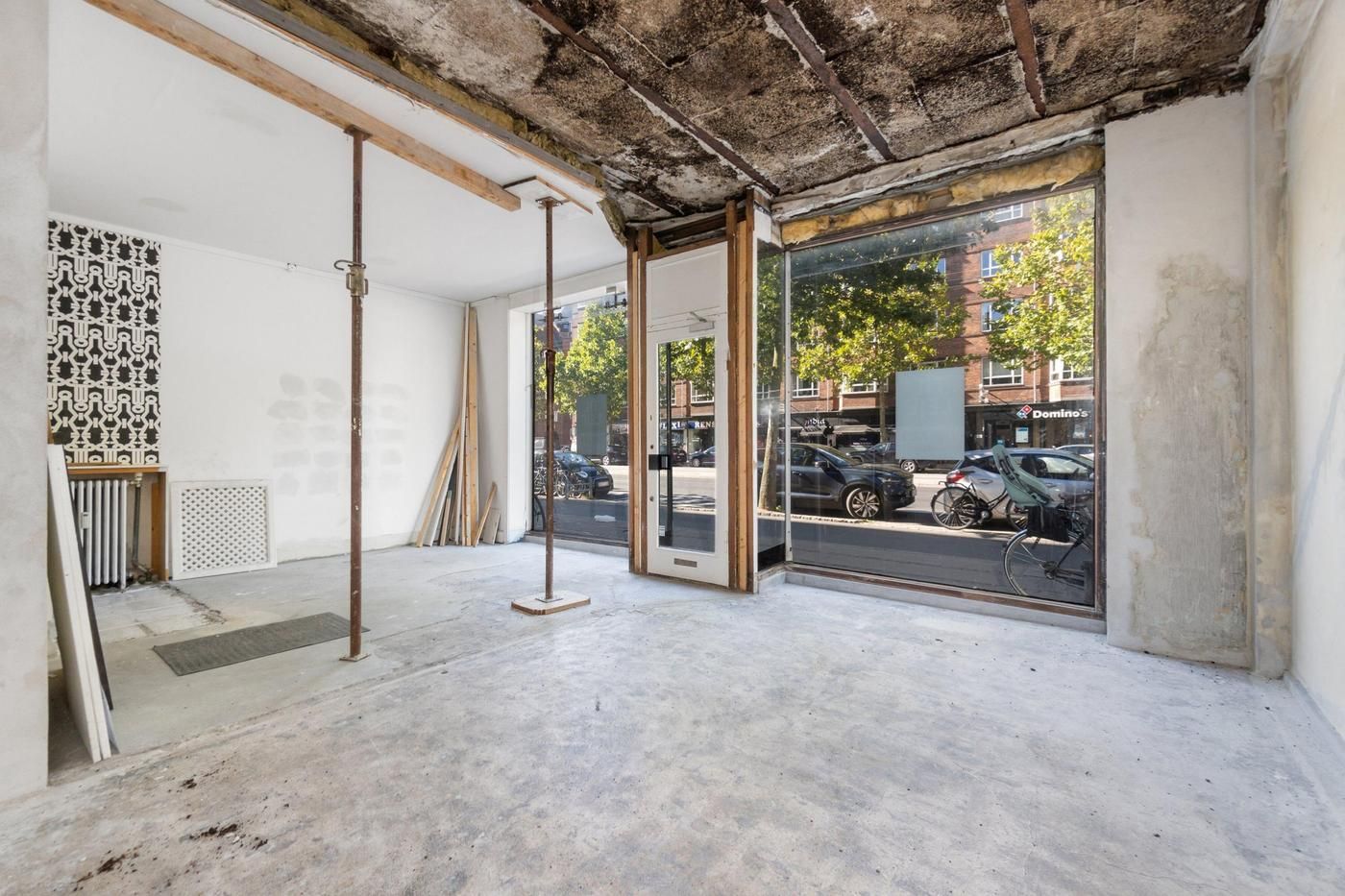 Store facadevinduer og tomme lokaler på Østerbrogade med udsigt til Domino's og parkeret bil og cykel