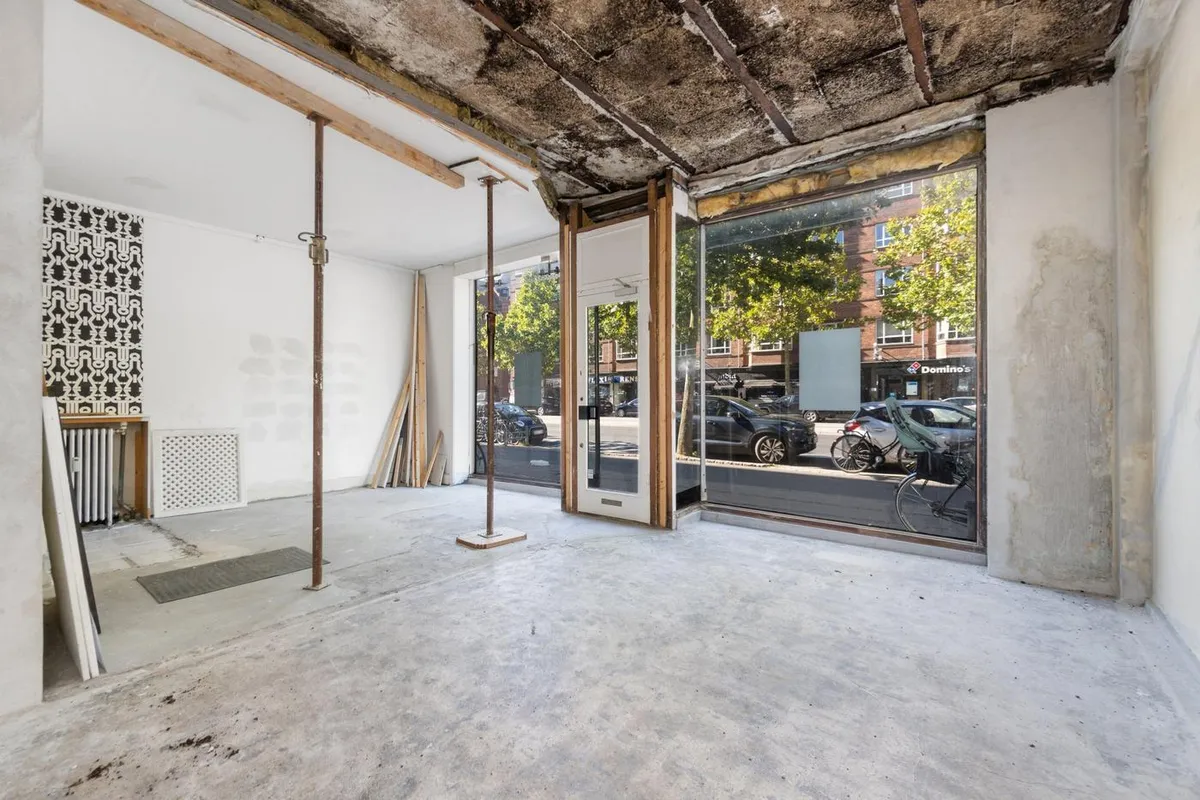 Store facadevinduer og tomme lokaler på Østerbrogade med udsigt til Domino's og parkeret bil og cykel