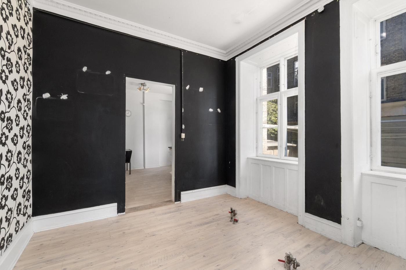 Et stort, tomt rum med hvide og sorte vægge, to store vinduer, hvor man kan se en gård udenfor, og to små plastikfigurer på