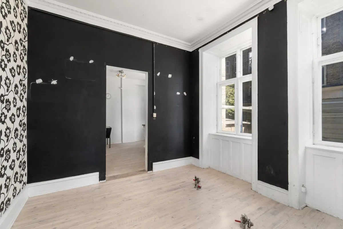 Et stort, tomt rum med hvide og sorte vægge, to store vinduer, hvor man kan se en gård udenfor, og to små plastikfigurer på