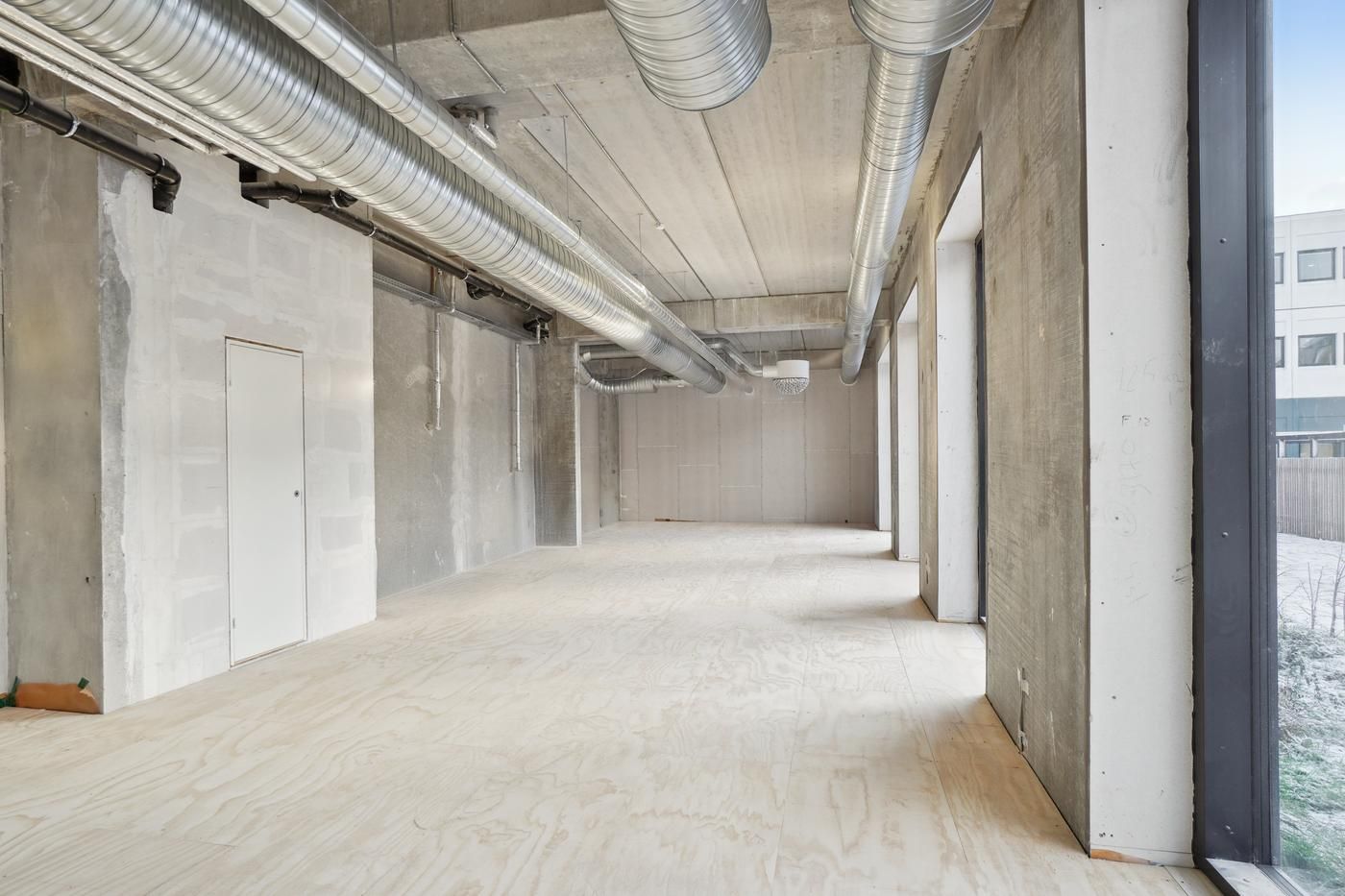 Indeni et stort, tomt værelse med pletfri, lyse trægulve og hvide vægge og loft med luftkanaler