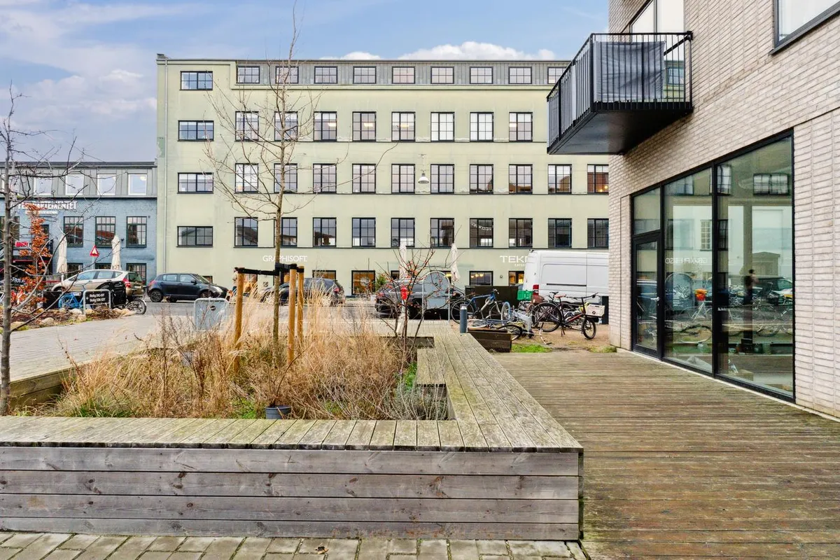 Rummeligt lejemål med terrasse i et moderne kvarter med lyse lofter, glasvinduer og udsigt til park.