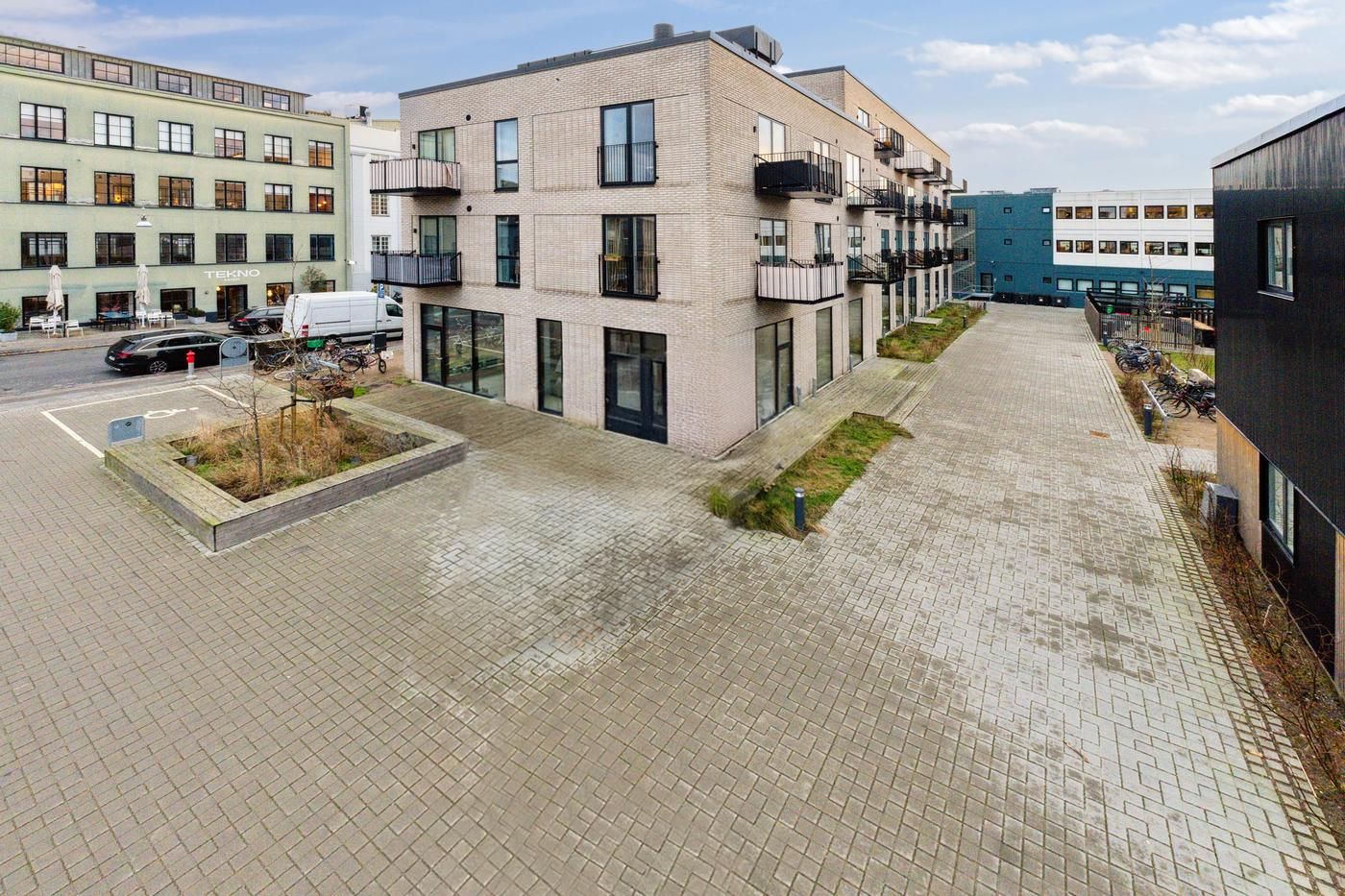 Moderne lejemål i en stor bygning med balkoner og grønne anlæg foran. Et rødt skriveord er synligt på facaden.