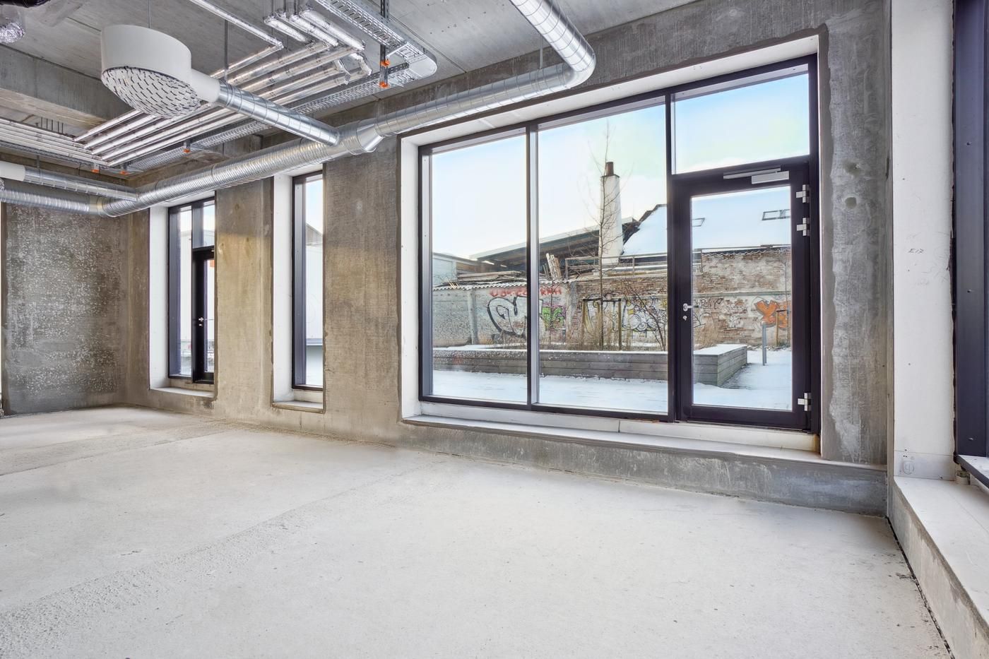 Rummeligt lokale med store vinduer og høje lofter og vinduer og graffiti på væggen og piper på loftet