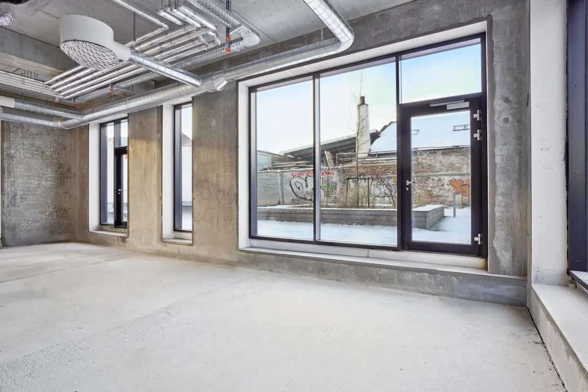 Rummeligt lokale med store vinduer og høje lofter og vinduer og graffiti på væggen og piper på loftet