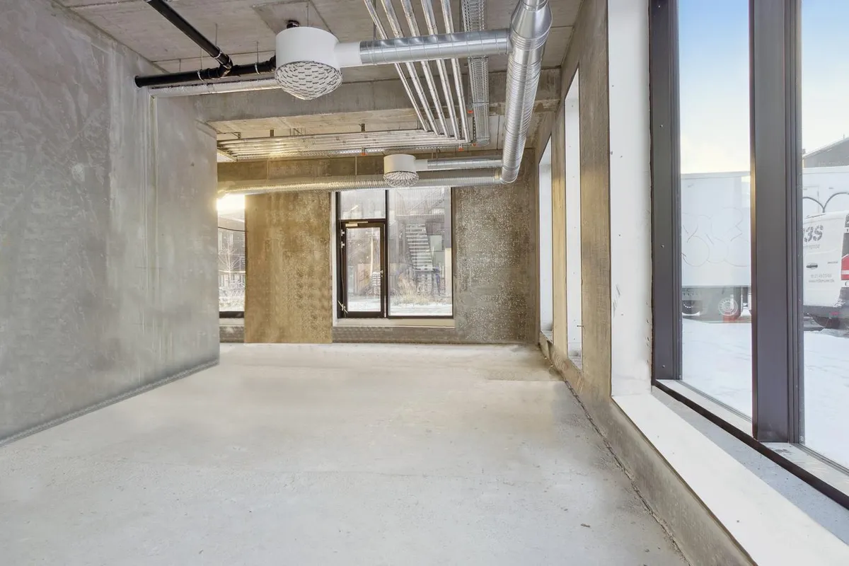 Store vinduer med skur udenfor, lysekroner og rør på loftet, store rum, og betonmure med skrald og graffiti