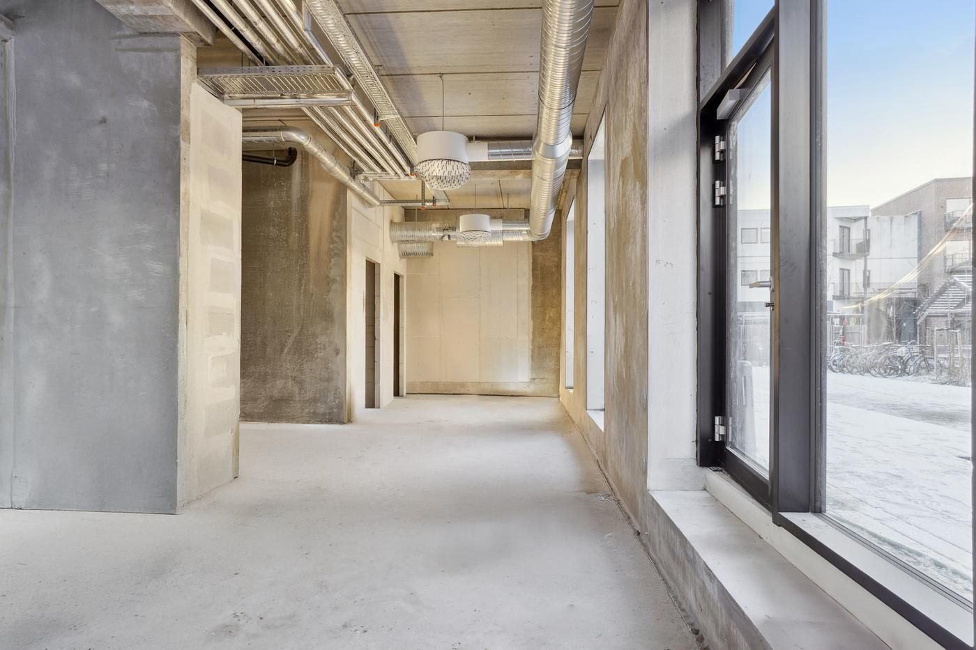 Moderne og rummeligt lejemål med højloftede rum og industrielle elementer, hvidgulve, og store vinduer med udsigt til en