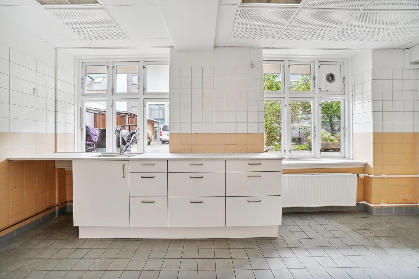 Lejlighed med køkken, gule og hvide vægge, vinduer med gardiner, radiator og moderne køkkenudstyret med en hvid ovn