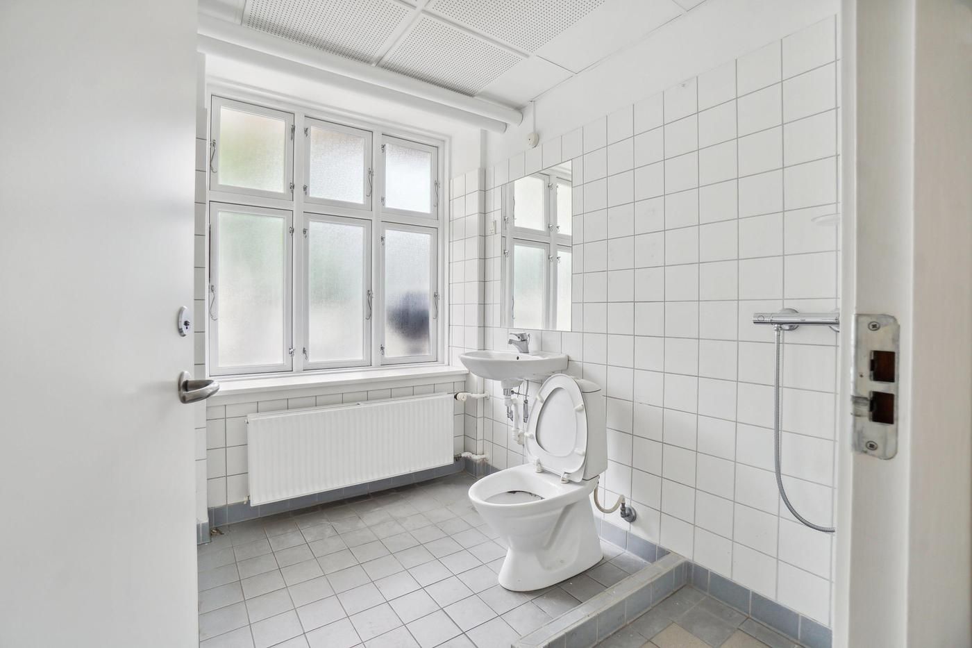 Et badeværelse med hvidt toilet, hvidt badekar, hvidt spejl og hvidt badekar med håndklæde.