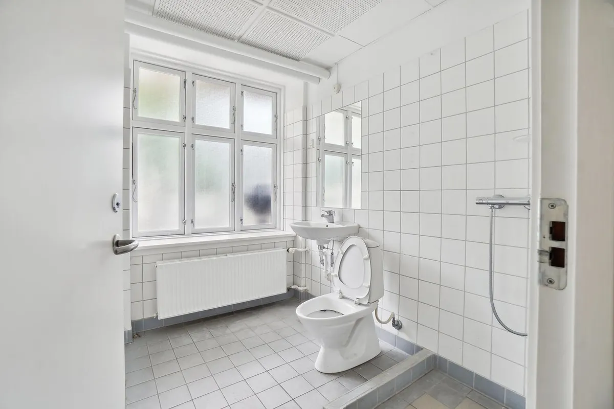 Et badeværelse med hvidt toilet, hvidt badekar, hvidt spejl og hvidt badekar med håndklæde.