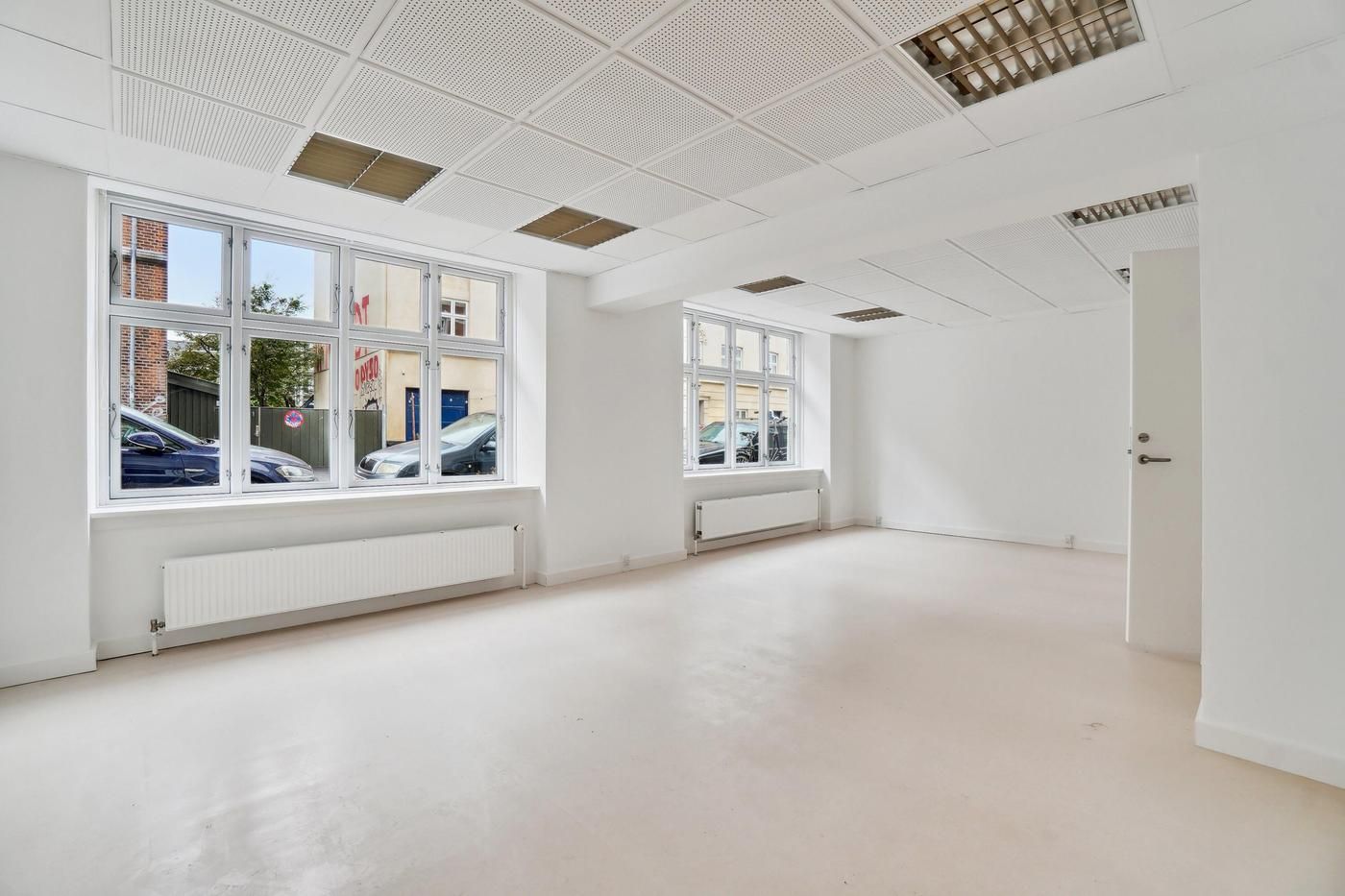 Et tomt kontor med hvide vægge og gulv samt store vinduer og radiatorer i væggene