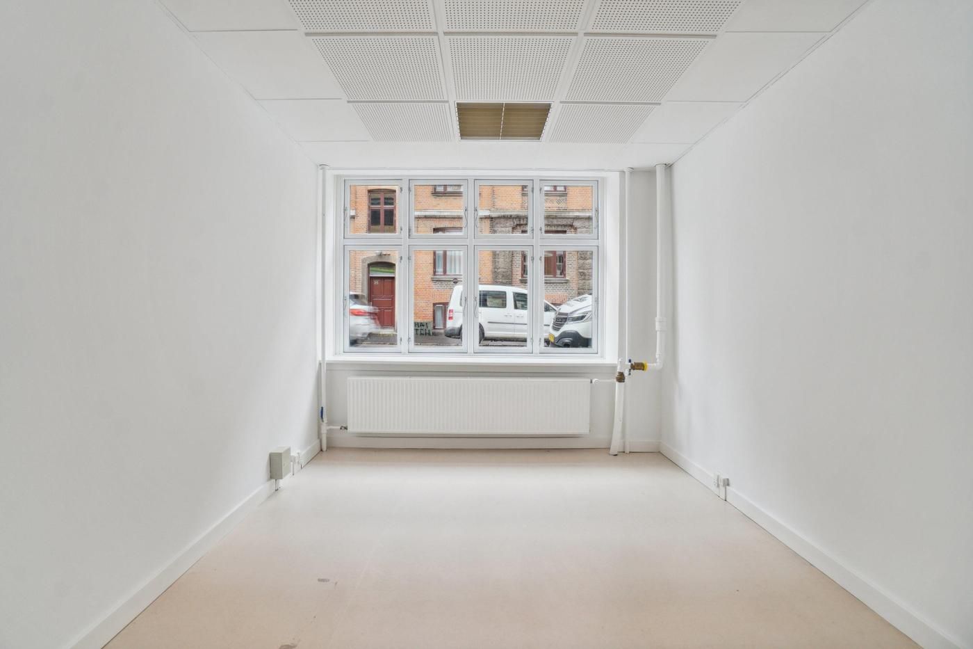 Erhvervslejemål med moderne design og stort vindue med udsigt til en gård og biler i baggrunden