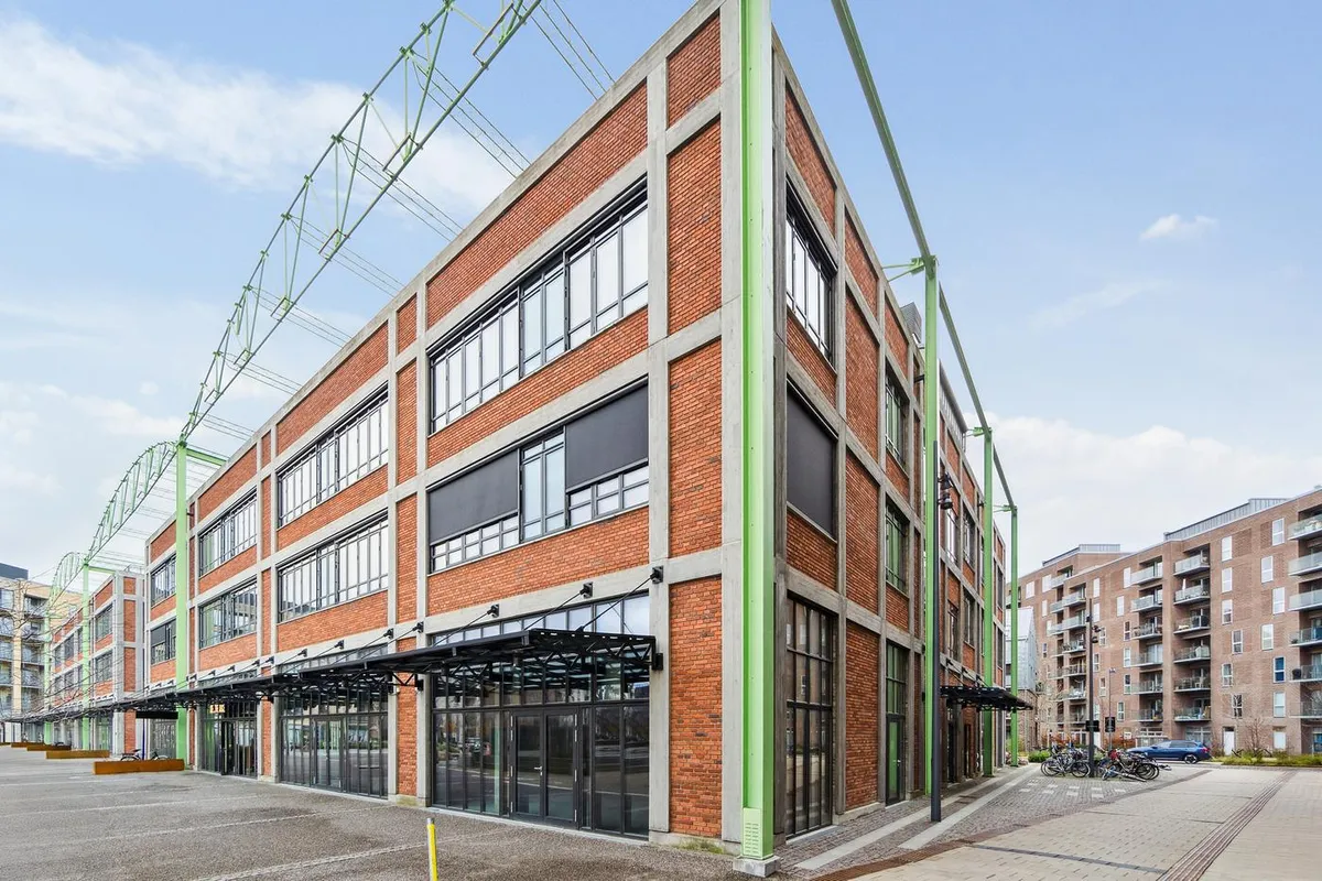 En stor bygning med mange vinduer og røde mursten samt grønne metalbjælker i Amsterdam