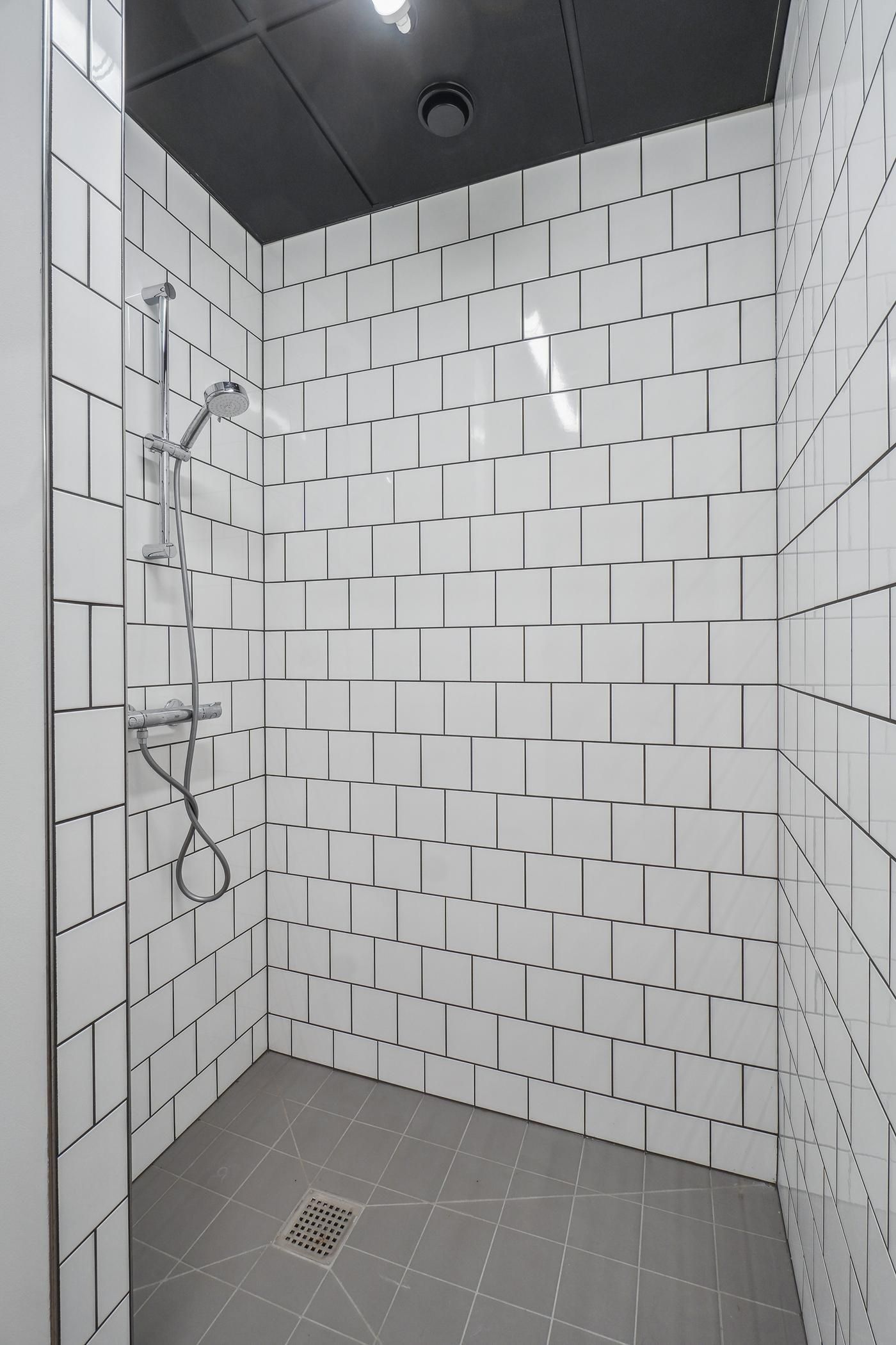 En hvidt kaflede badeværelse med gulv og loft samt en hængende bruser med slange og vandhane