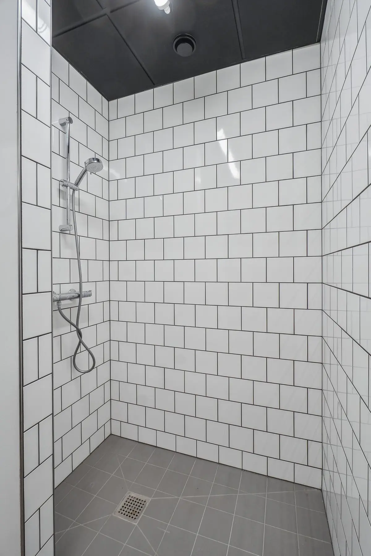 En hvidt kaflede badeværelse med gulv og loft samt en hængende bruser med slange og vandhane