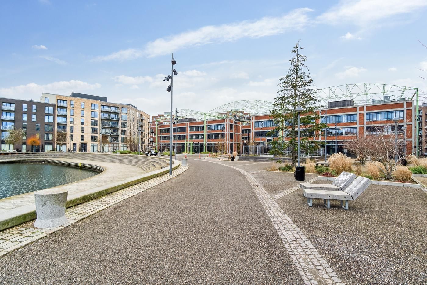 Vej langs vand med udsigt til bygninger og kontorer med glasvinduer og to bænke i vejen