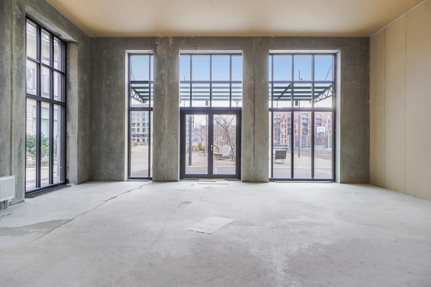 Ledig lokale med tre store vinduer og dobbeltdøre i en bygning med en industriel stil og udendørs terrasse