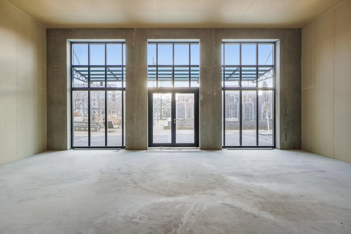 Store glasvinduer med dobbeltdøre i en moderne, industriel bygning med betonvægge og en tom rumindretning