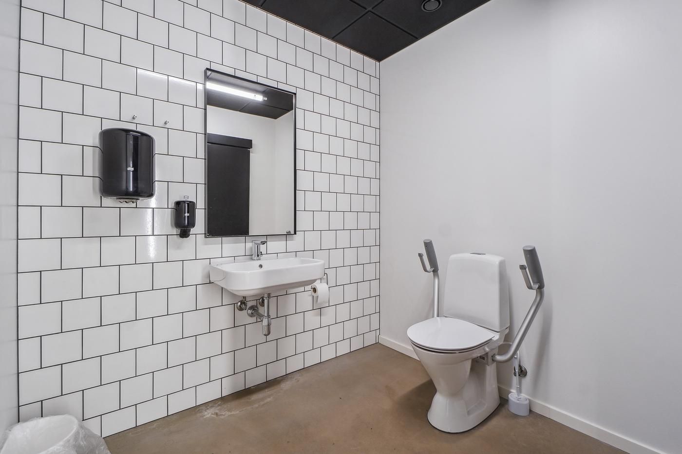 Rent og moderne toilet med hvid keramik og højloftede lofter, toilet med håndtag til støtte og håndsæbe dispenser på væggen