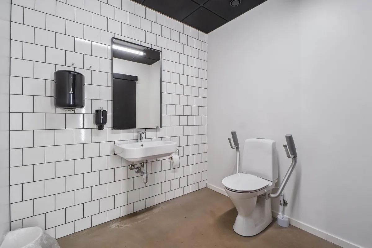 Rent og moderne toilet med hvid keramik og højloftede lofter, toilet med håndtag til støtte og håndsæbe dispenser på væggen