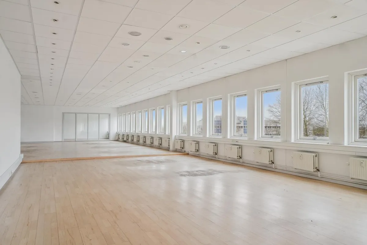 Lyst kontorrum med lysegul gulvbelægning og hvide vægge og loft. Rader af store vinduer og spejle langs væggen.