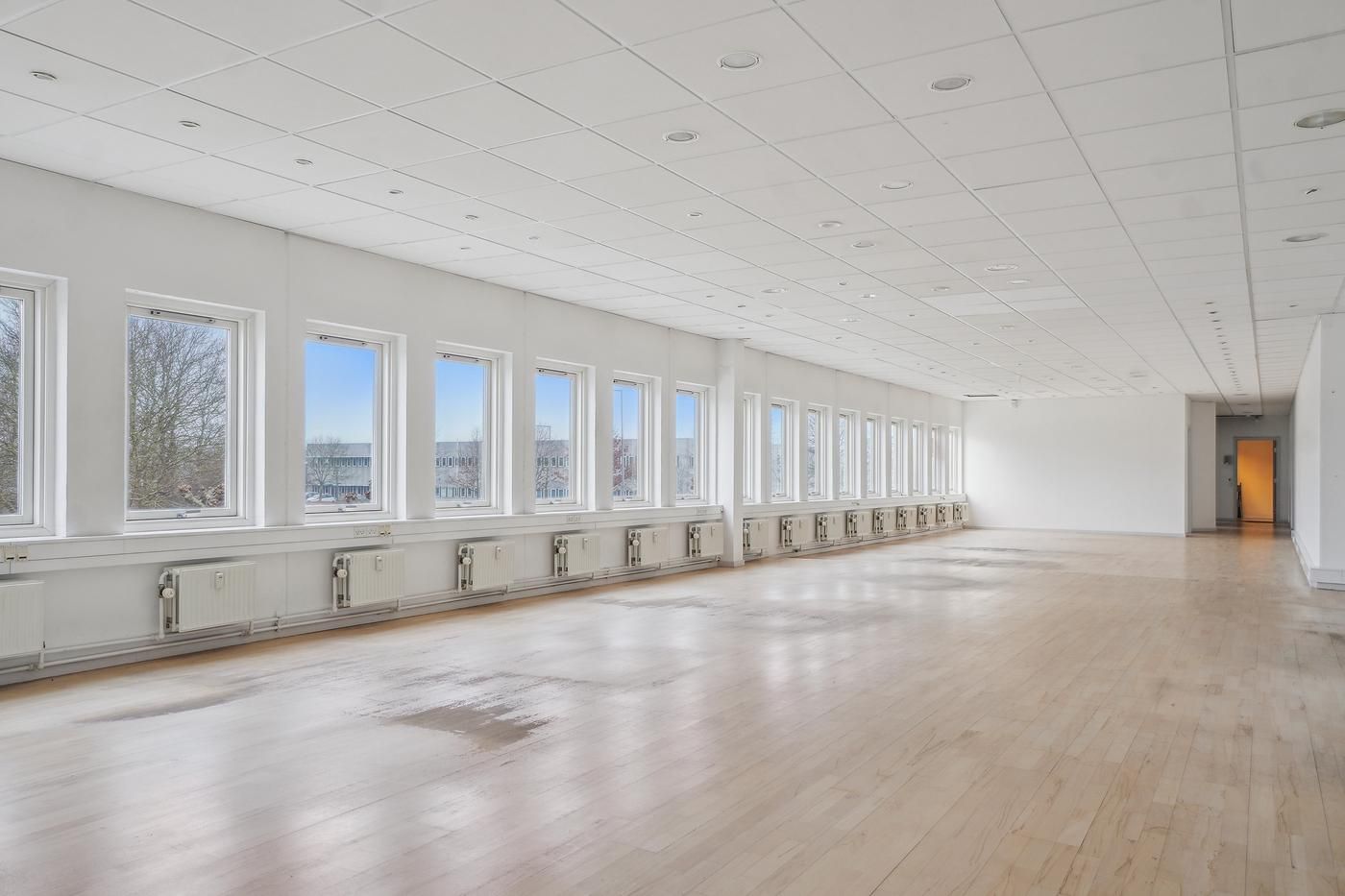 Store rummeligt og velholdt kontor med store vinduer og hvide vægge og loft samt parketgulve