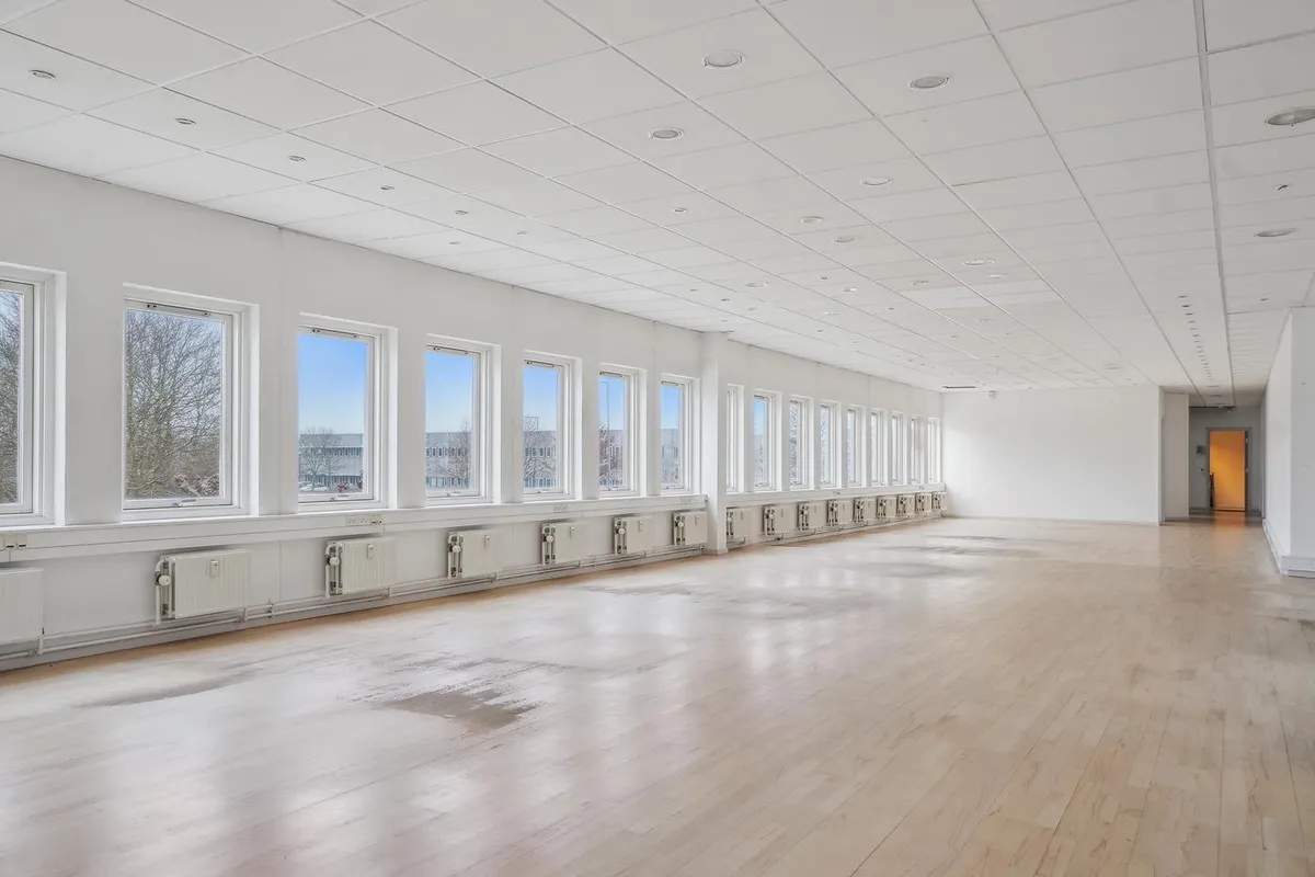 Store rummeligt og velholdt kontor med store vinduer og hvide vægge og loft samt parketgulve