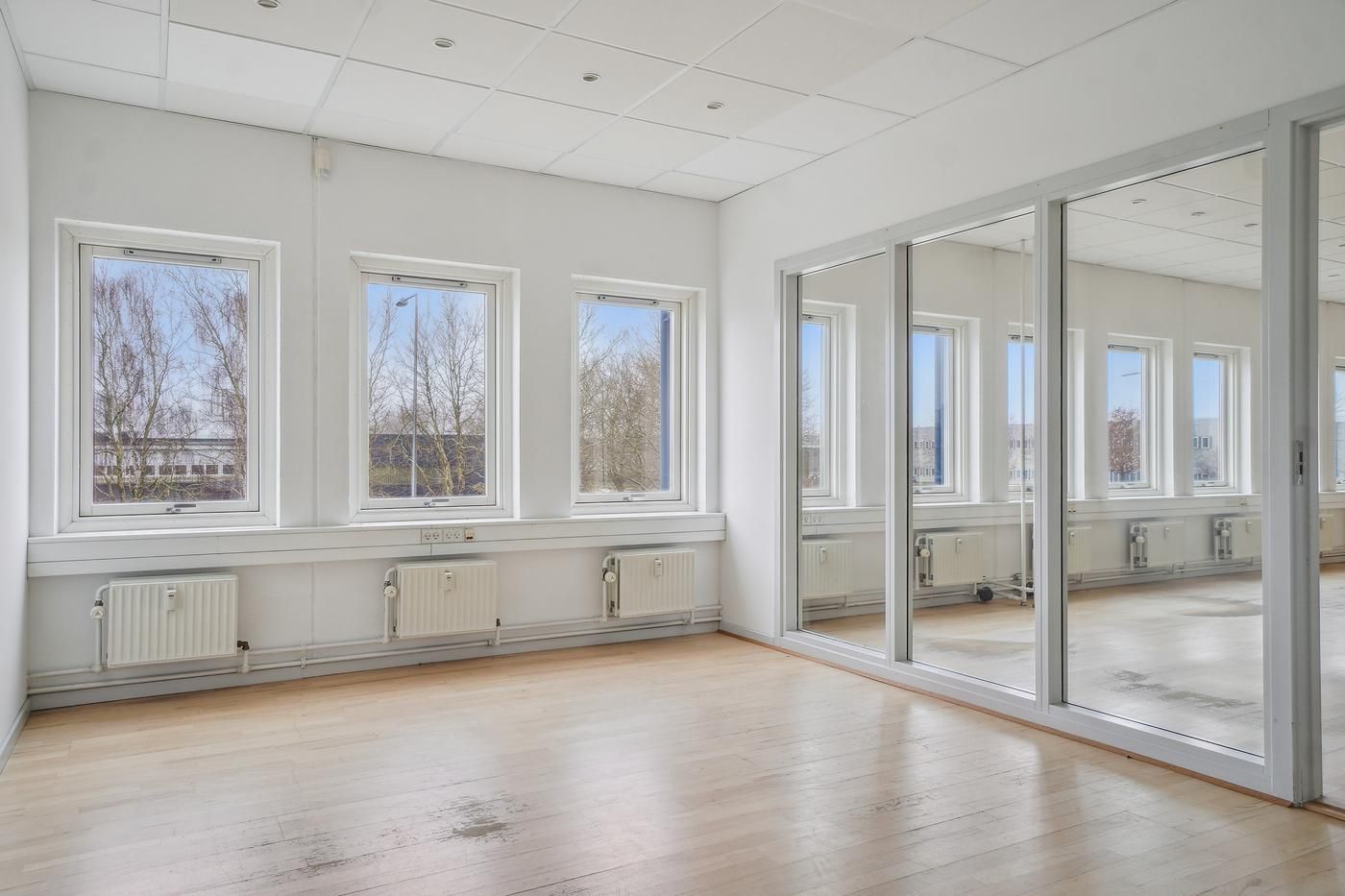 Et stort, lyse og velholdt kontorlokale med glasvinduer, hvide vægge og trægulv samt stålskiltene med håndtag