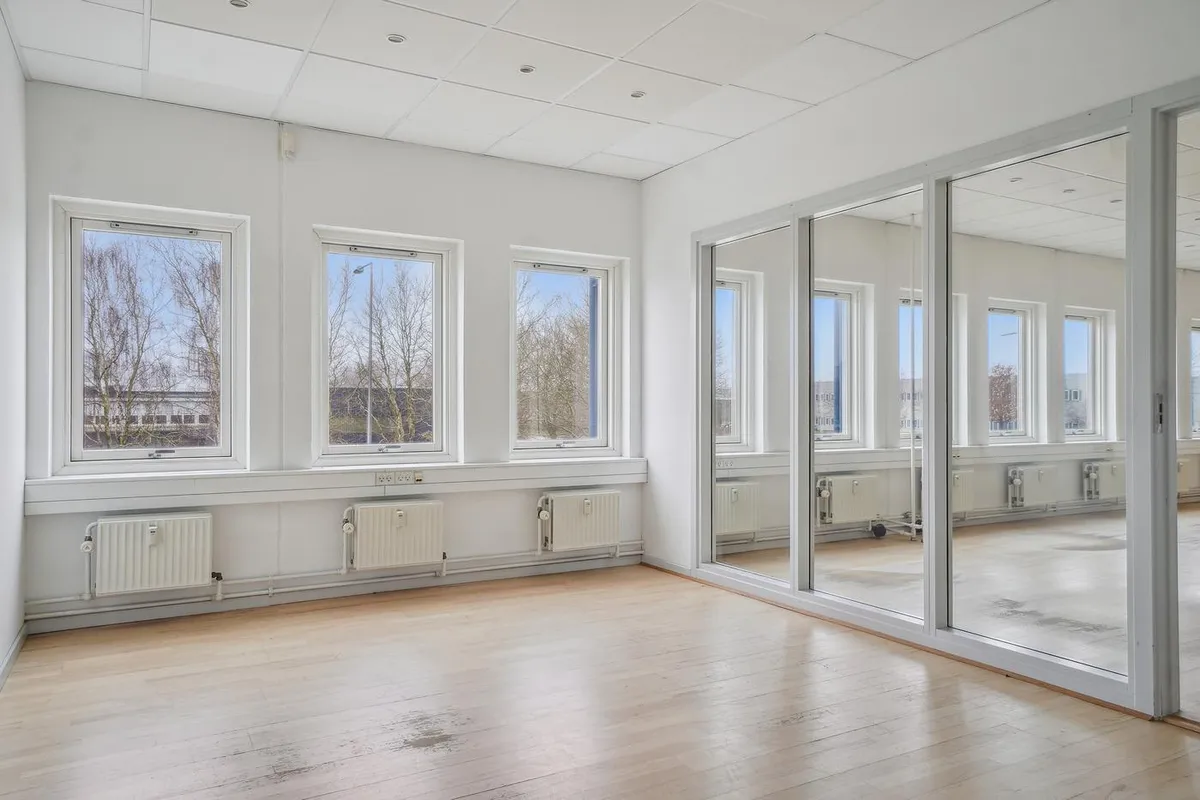 Et stort, lyse og velholdt kontorlokale med glasvinduer, hvide vægge og trægulv samt stålskiltene med håndtag