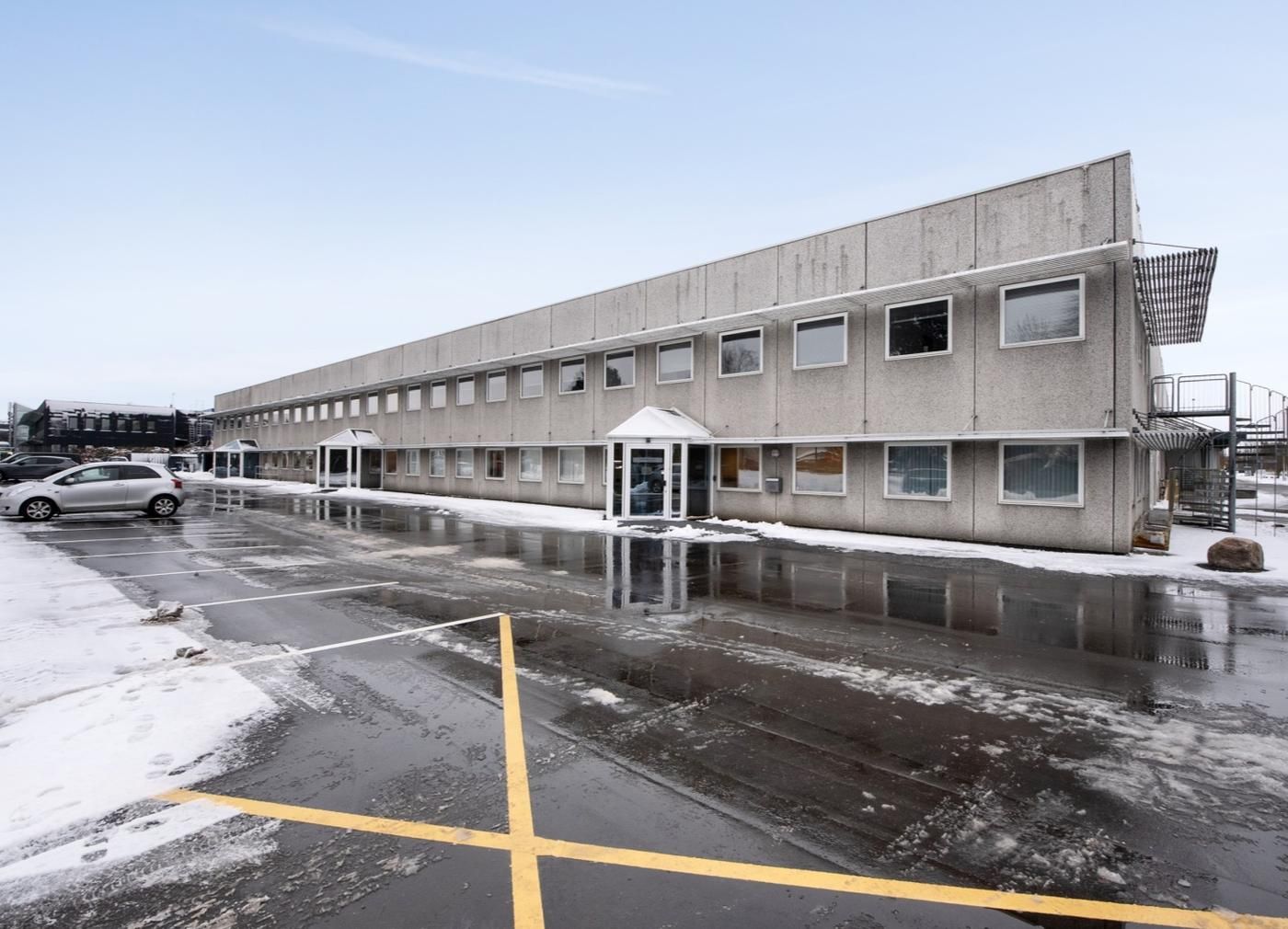 Parkeringsplads med vandspor og sne foran kontorlokaler med store ruder og glasdøre