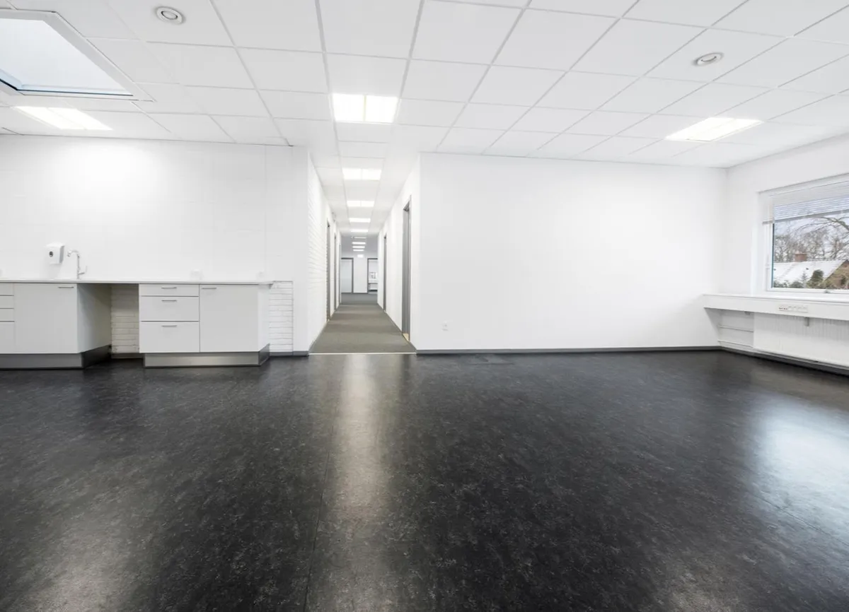 Korte gange med hvide vægge og gulv i et moderne kontor med et vinduesparti og hvidt loft