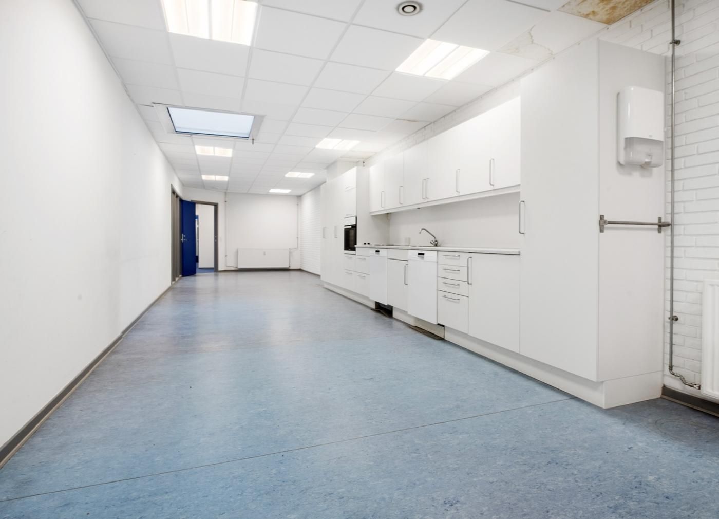 Moderne og pænt kontorlokaler med hvide vægge og loft samt højloftede loftsplader. Komplet med hvide køkkenskabe og en blå