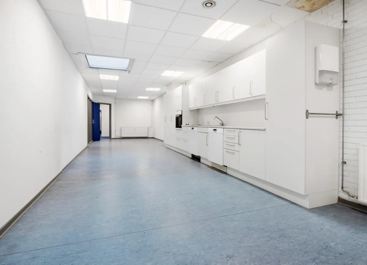 Moderne og pænt kontorlokaler med hvide vægge og loft samt højloftede loftsplader. Komplet med hvide køkkenskabe og en blå