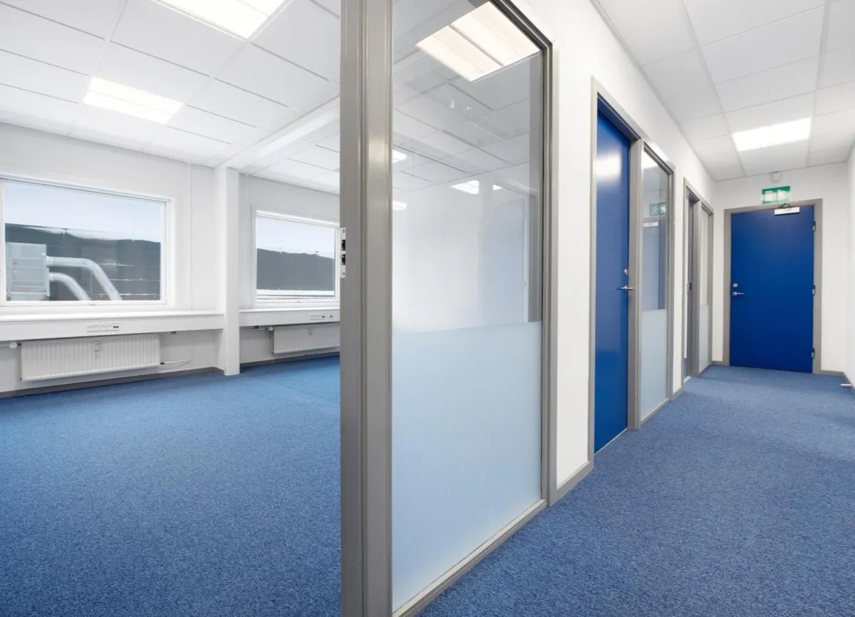 Kort kontorlokaler med blå gulv, hvide vægge og blå døre samt vinduer og indbygget radiator under vinduet