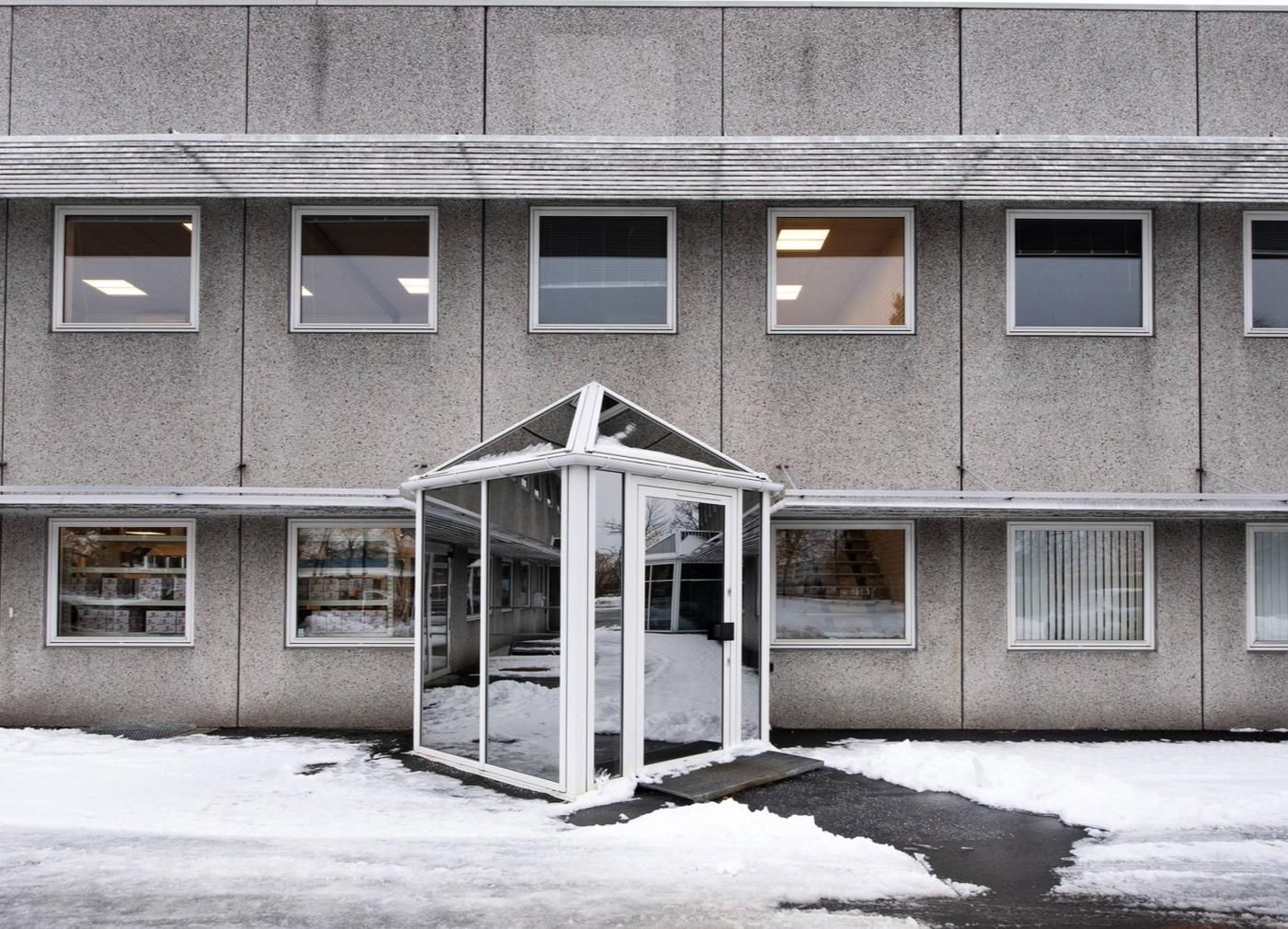Kontorbyggeri med glasvinduer og snedækket foran. En åben glasgang er forsynet med en lille rampe og sne foran.