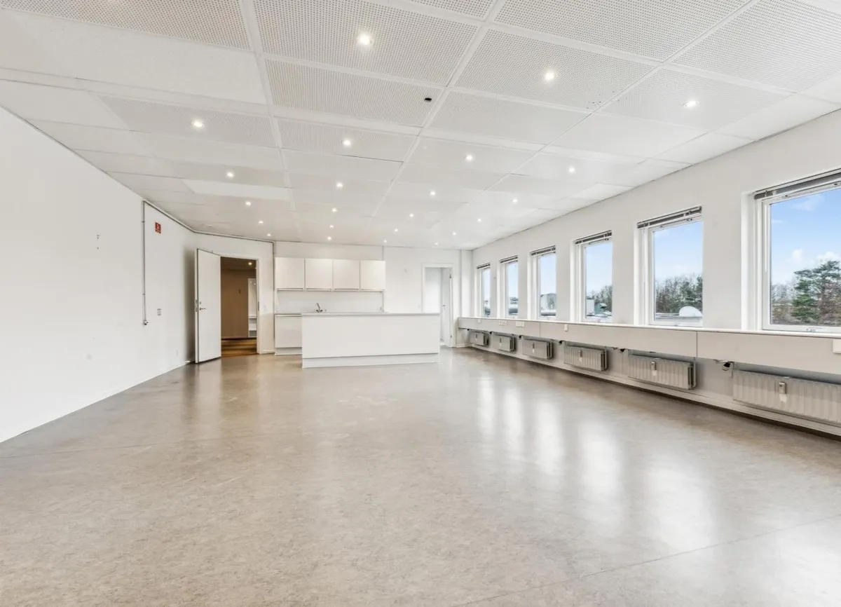 Kontorrum med hvide vægge, gulv og loft, hvor der er vinduer med udsigt til træer og blå himmel