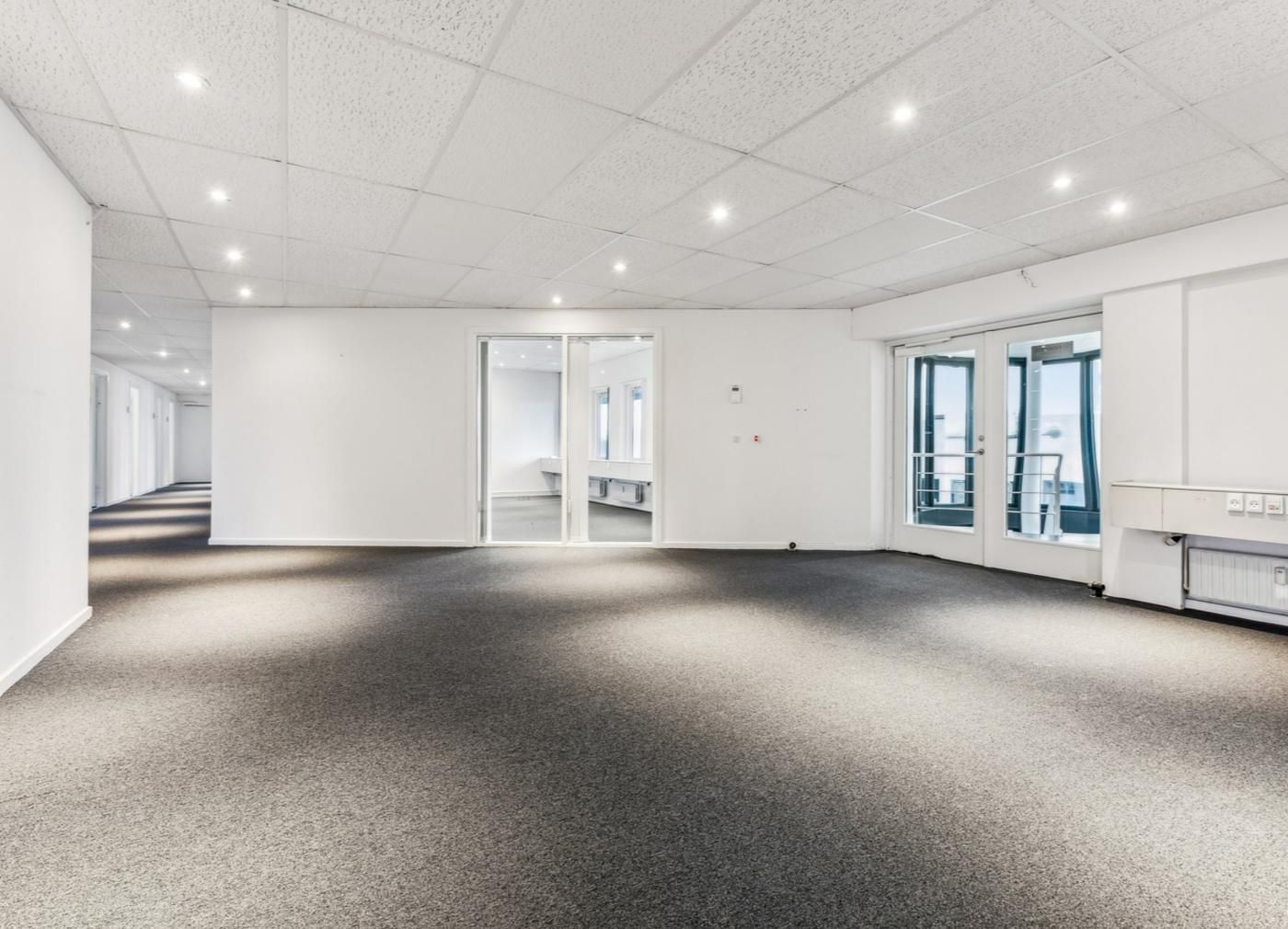 En stor, tom, hvid kontorvirksomhed med to vinduer og åbne døre til et mødelokale med højt loft