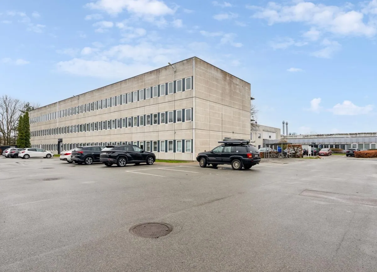 På parkeringspladsen er der fem parkerede biler, og der er et kørespor i midten