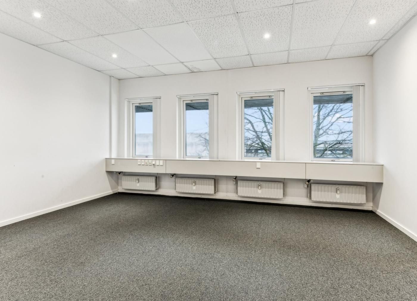 Kontor med fire vinduer og radiatorer under, moderne og velplejet design, lyst og rummeligt