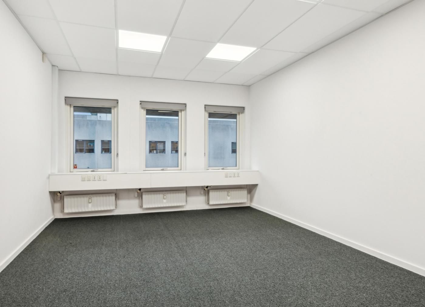 Store kontorlokaler med hvide vægge, hvide lofter, tre vinduer og tre radiatorer langs væggen