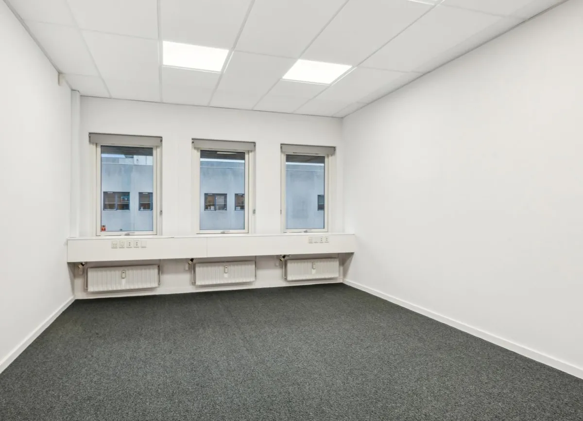 Store kontorlokaler med hvide vægge, hvide lofter, tre vinduer og tre radiatorer langs væggen