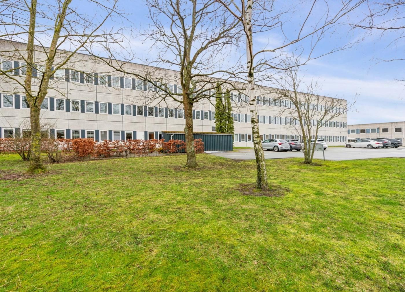 Kontorbyggeri i Skovlunde med grønne områder og parkeringsplads for biler
