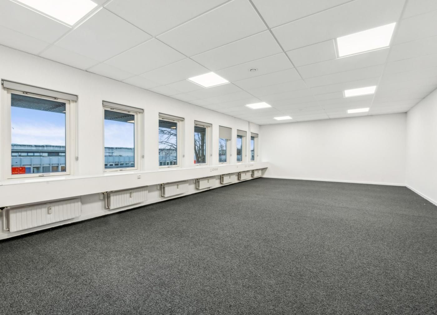 Store kontorlokaler med mange vinduer og hvide vægge samt højloft og lyse loftslampe lys.