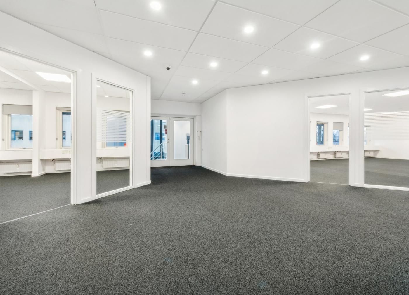 Det er en stor og ren kontorhall med hvide vægge og lofter samt højkvalitets gulvbelægning. Der er flere spejle og vinduer,