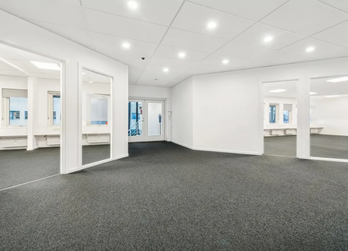 Det er en stor og ren kontorhall med hvide vægge og lofter samt højkvalitets gulvbelægning. Der er flere spejle og vinduer,