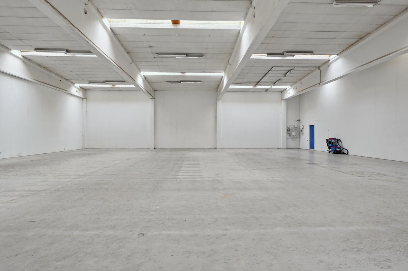 Tomt, velholdt lagerrum med hvide vægge og lyse gulv samt åbne vinduer i loftet og en dør til siden