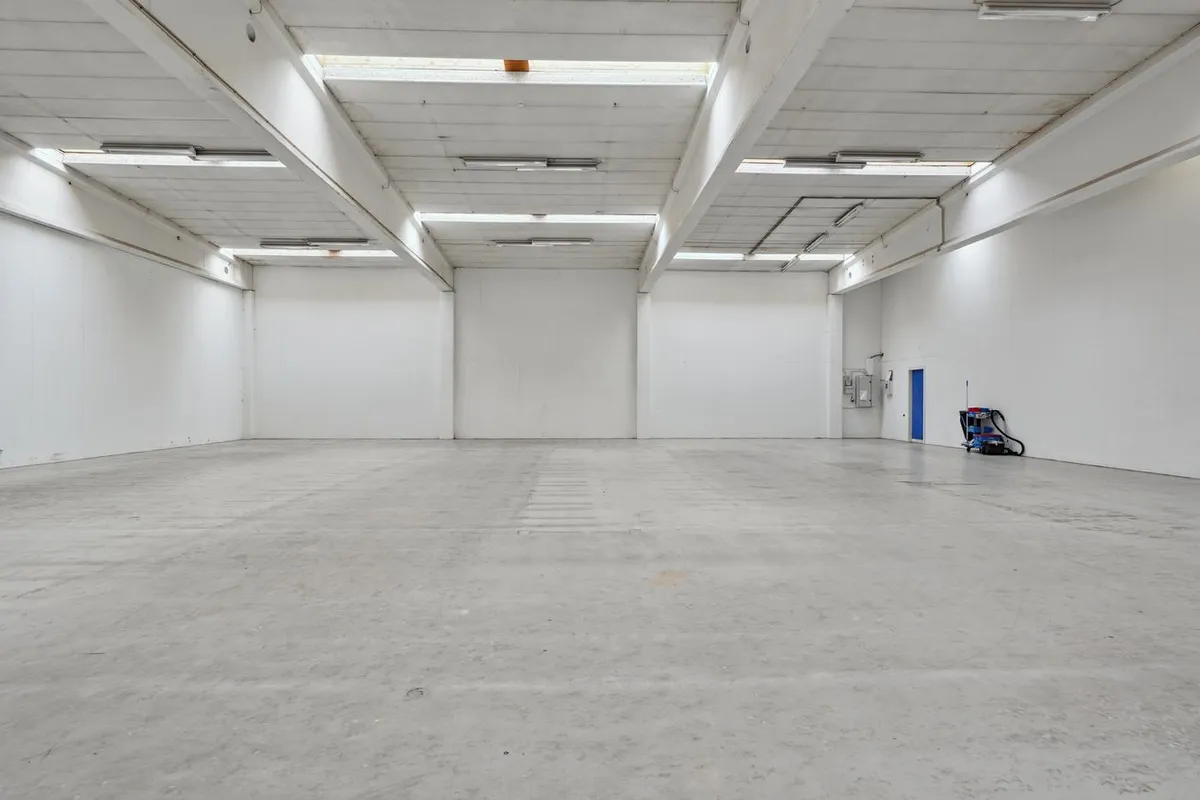 Tomt, velholdt lagerrum med hvide vægge og lyse gulv samt åbne vinduer i loftet og en dør til siden