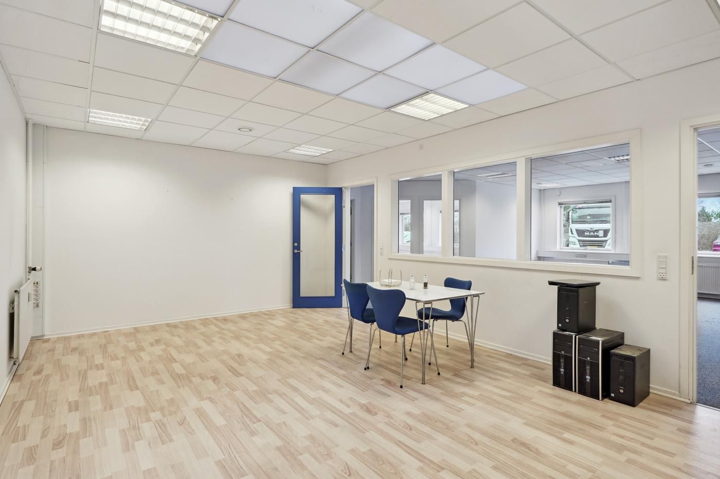 Rummelig kontor med hvide vægge, lyse gulvbelægning og store vinduer samt møbler og computere