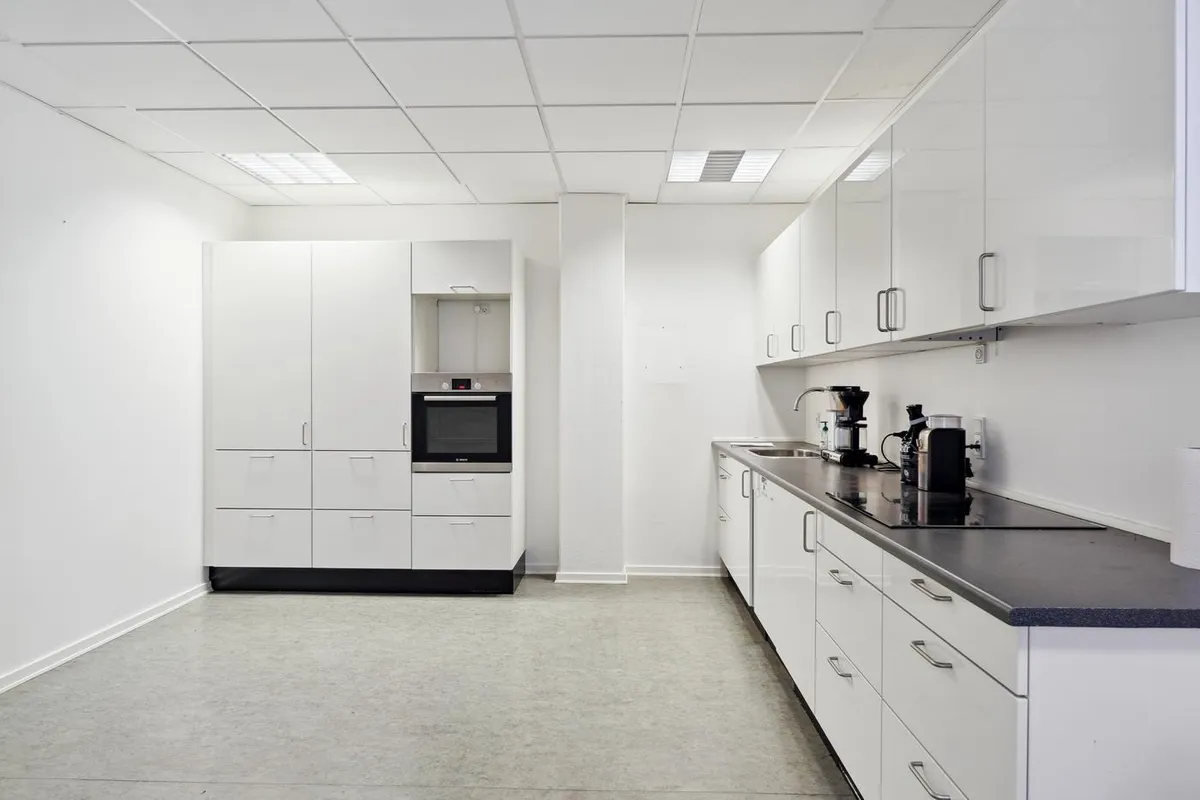 En tom kontorkøkken med hvide vægge, højloft og køkkenudstyret og -møbler i hvid og sort.