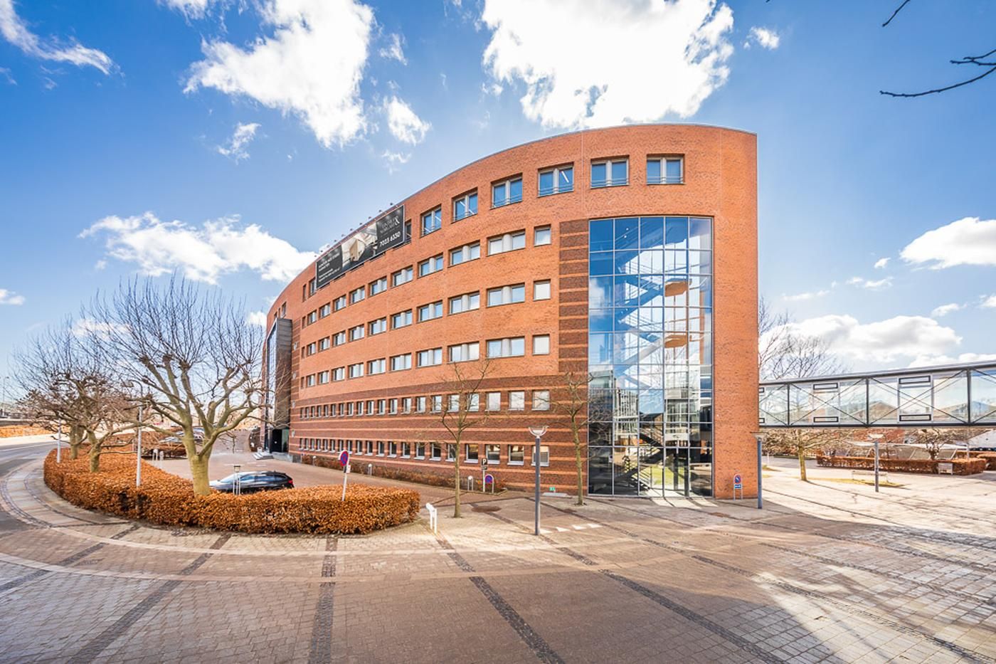 Moderne kontorbygning med gul tegl og glasvinduer i Kongens Lyngby, parkeringsplads og gåbro